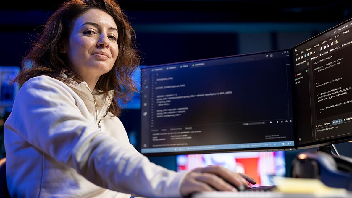 female computer anaylst sitting in front of a computer monitor smiling at the camera