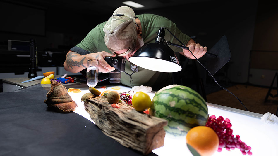 male student wearing a backwards baseball cap photographing fruit