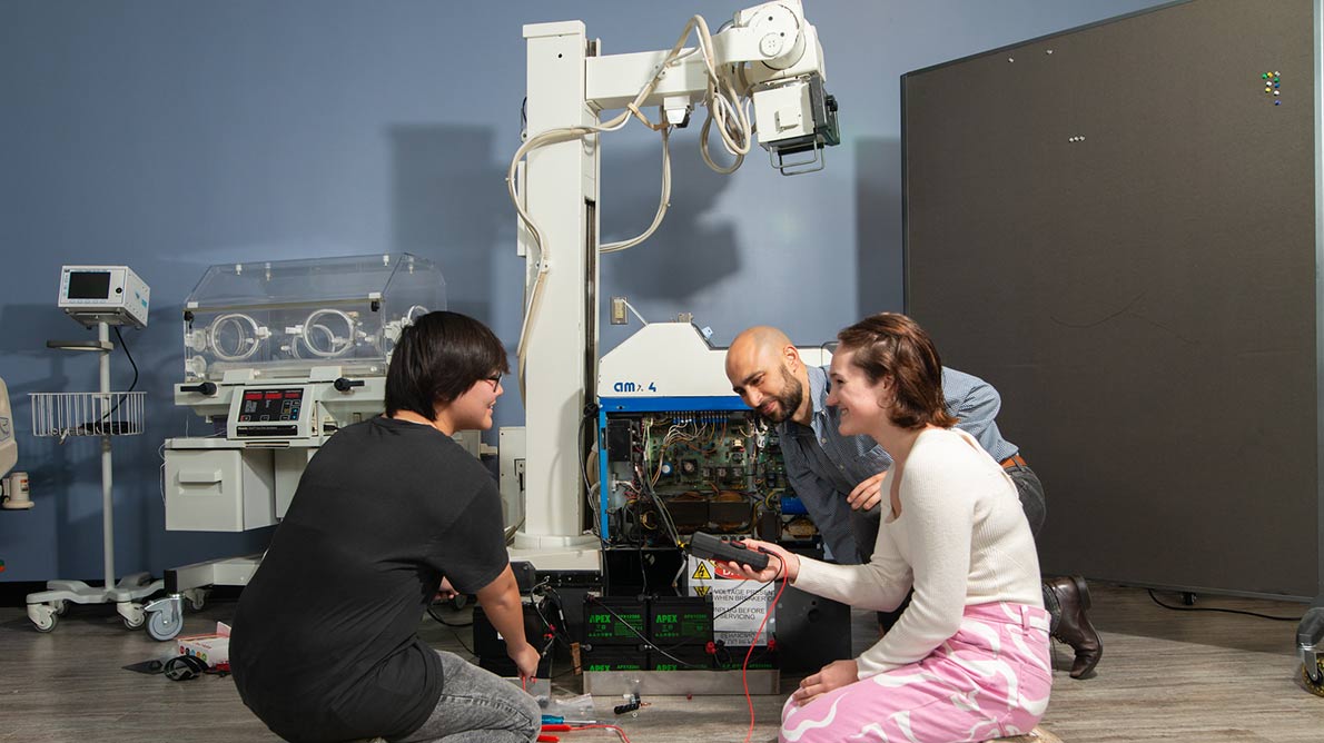 male student, SPC Professor Brian Bell and a female student working on a biomdical machine