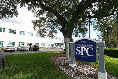The SPC Epi-Services building pictured behind tall oak trees, with the blue SPC sign in the foreground.