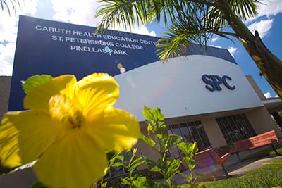 The SPC Health Education Center pictured behind a close-up of a yellow flower, a palm tree, and under a blue sky with white clouds.