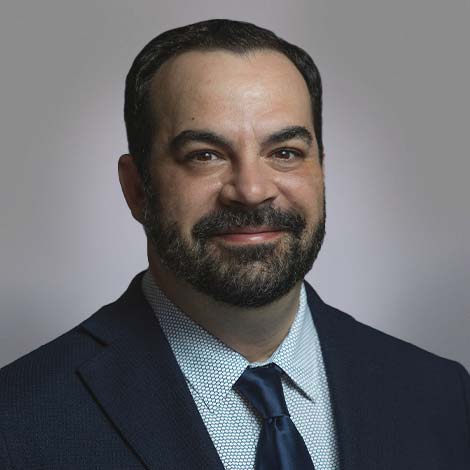 A portrait of Richard RJ Jacques, wearing a blue suit coat and tie.