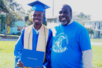 SPC graduate wearing regalia standing next to older man smiling