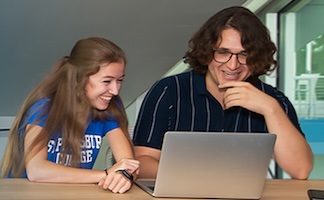 female and male students laughing while sharing a laptop