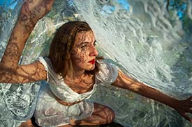Student digital media project. Photograph of a woman crawling under a swath of white lace fabric. The lace patterning covers her in intricate shadows.