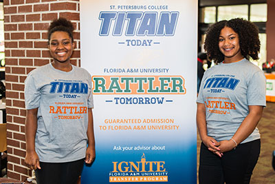 2 IGNITE program students posing in front of a poster 