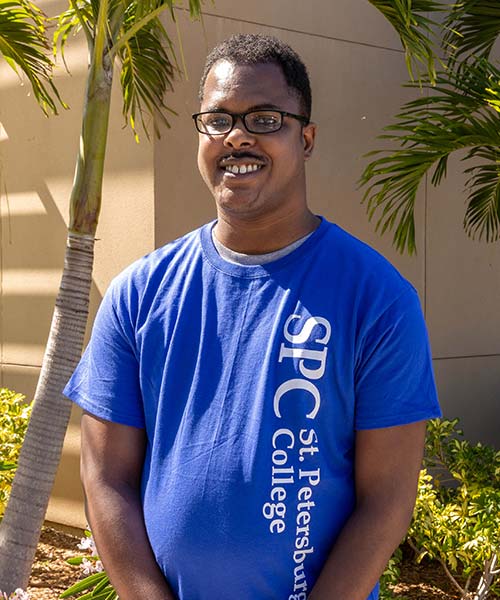 SPC alum Terry Ellison, standing in front of the palm tree landscaping of an SPC campus building, wearing a blue SPC T-shirt.